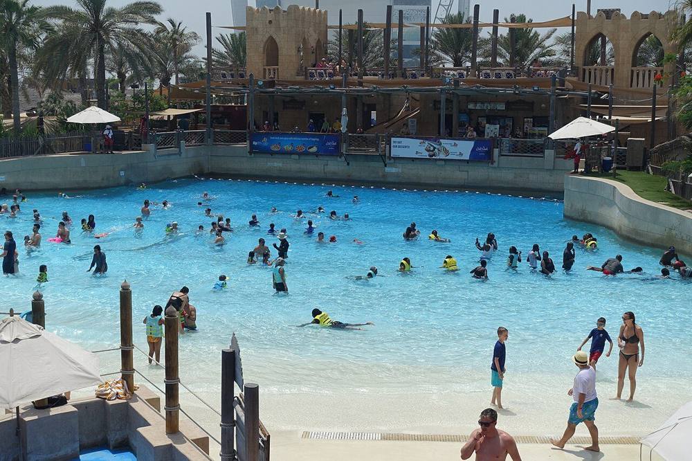 A busy wave pool at a water park, with swimmers and some children in life vests