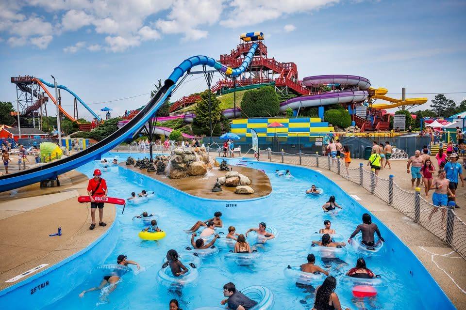 Visitors floating on tubes in a lazy river with tall water slides in the background
