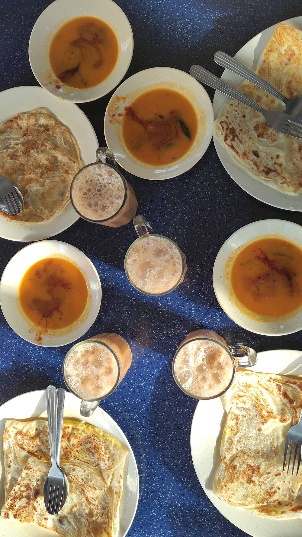 Roti canai served with curry dipping sauce beside a glass of teh tarik