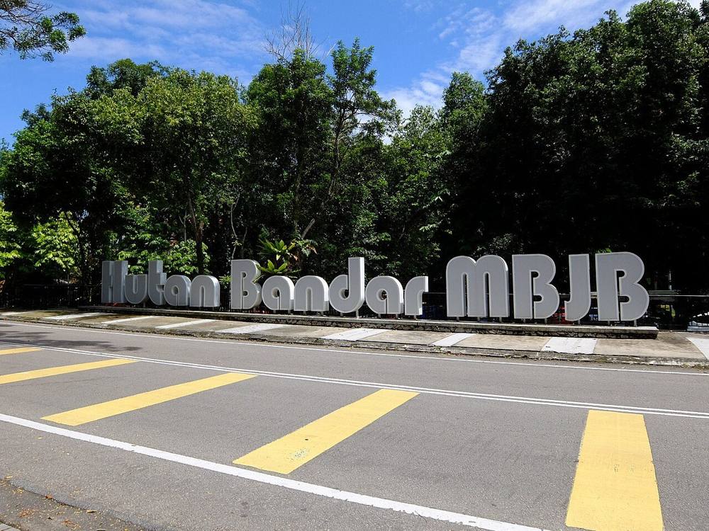 The Hutan Bandar MBJB sign at the roadside entrance, framed by tall trees