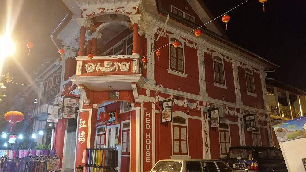 The Red House, a red and white heritage corner shophouse on Jalan Tan Hiok Nee, lit up at night with red lanterns