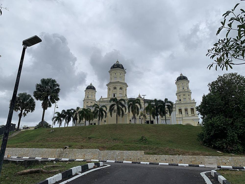 Sultan Abu Bakar State Mosque on a hill under a cloudy sky, with cream towers and dark domes