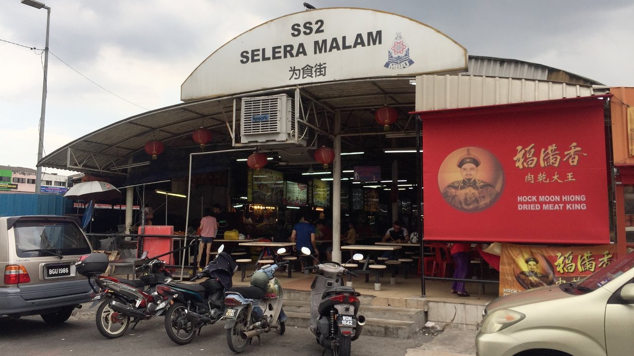 Open-air Malaysian hawker centre with dozens of food stalls and communal seating at night
