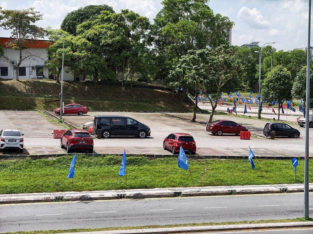 Blue party flags beside an empty car park and road in Larkin, Johor Bahru, during the 2026 state election period