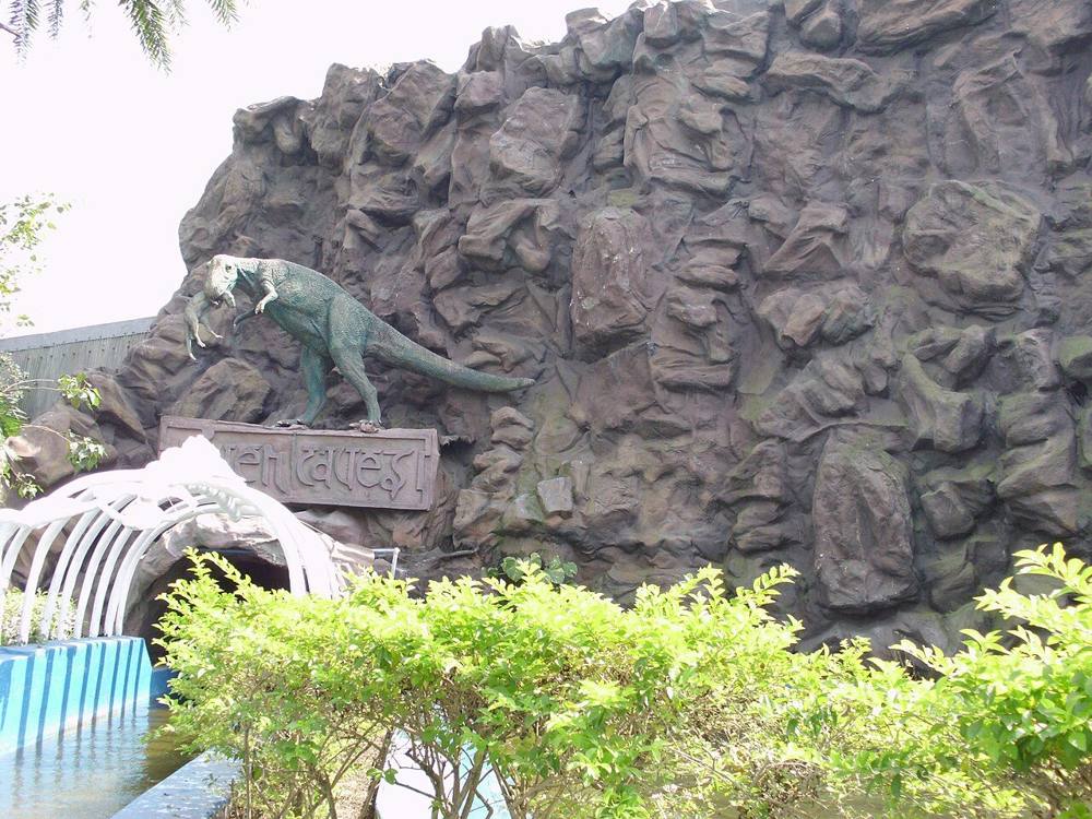 A dinosaur model on a rock wall beside a water ride at a theme park