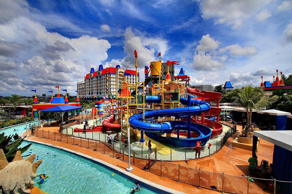 The colourful water park at LEGOLAND Malaysia with blue and red slides, a splash area and the resort hotel behind