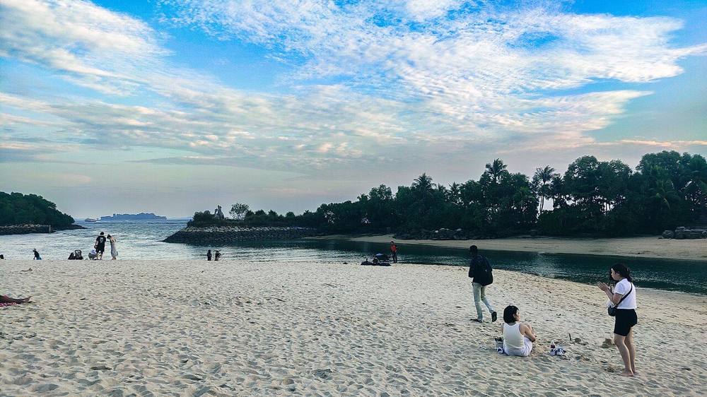 Palawan Beach on Sentosa at dusk with white sand, a few visitors and a tree-lined shoreline